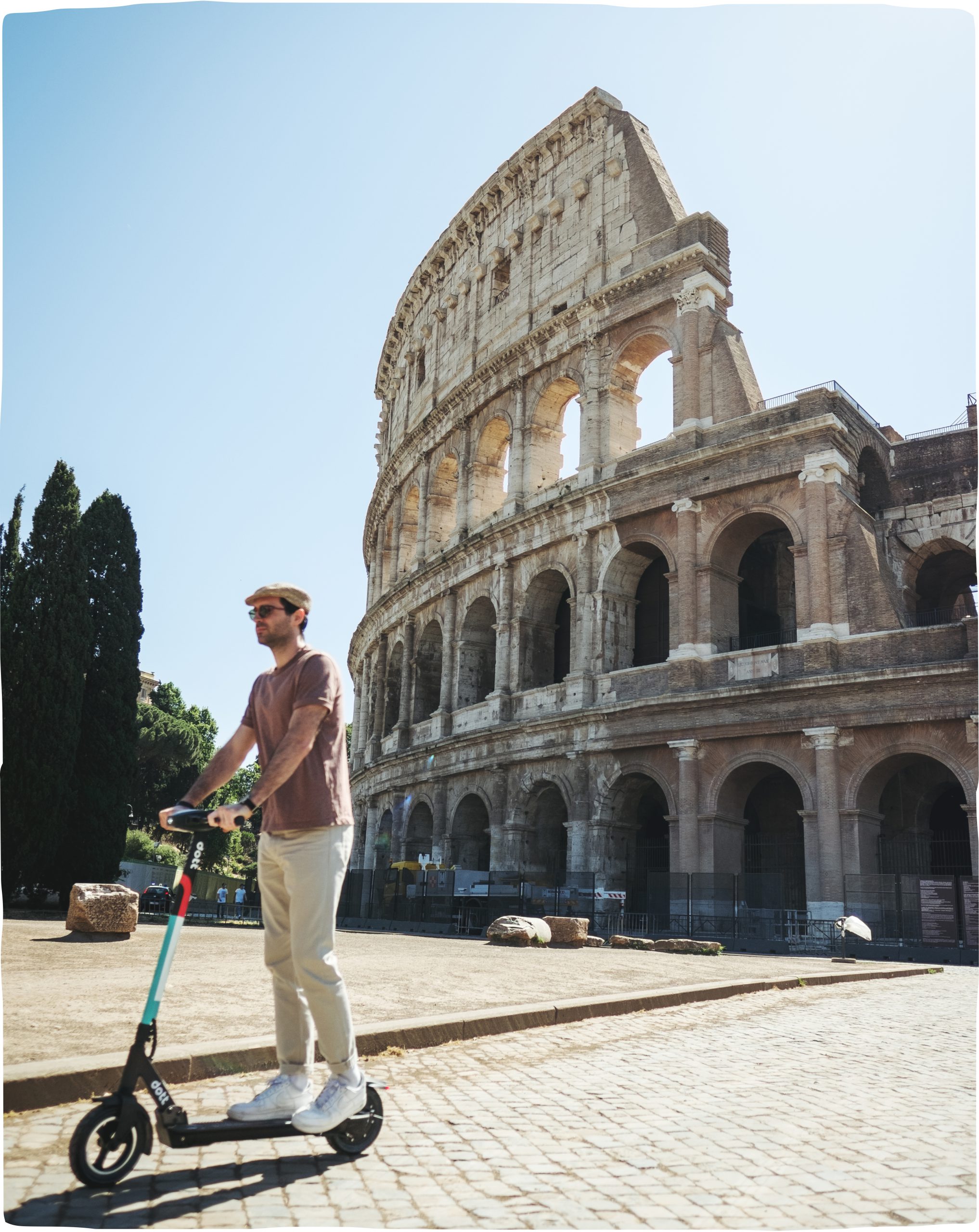 A man riding a scooter on a sunny day in front of the Colosseum in Rome.