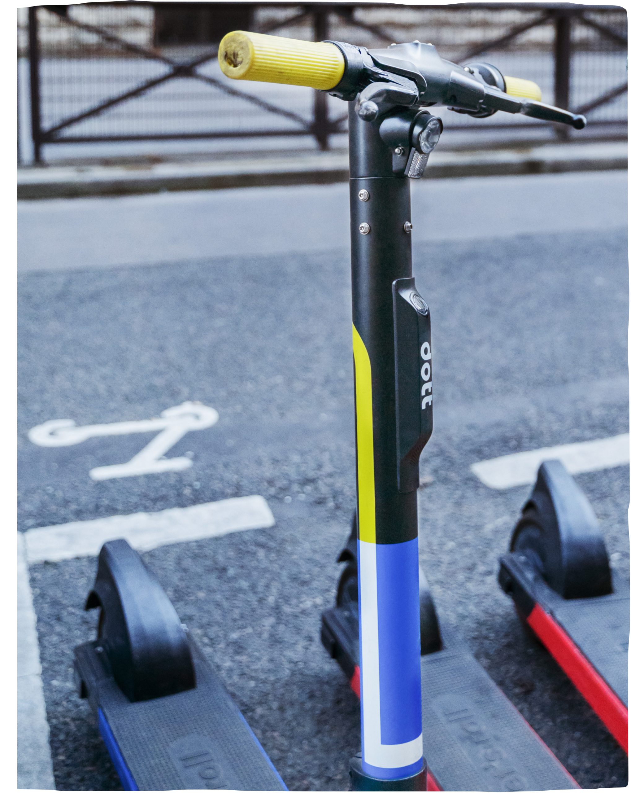 An image of a Dott e-scooter is in the middle of the frame. In the bottom right of the picture, two other Dott e-scooters are visible.