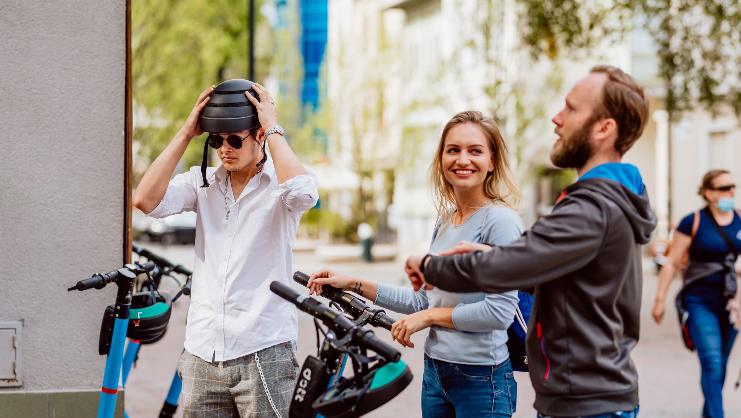 A group of three people laughing and putting their helmets on to get ready to ride Dott e-scooters.