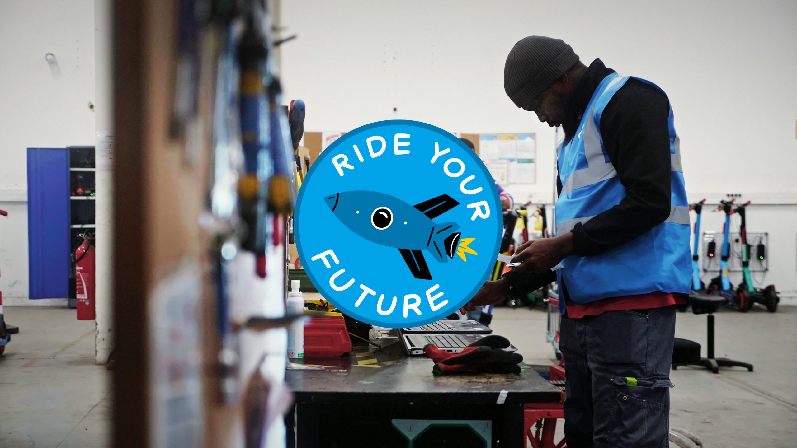 An image of a man working on a laptop in the Dott warehouse, with an illustration of a rocket encircled by the text ‘Ride Your Future’.