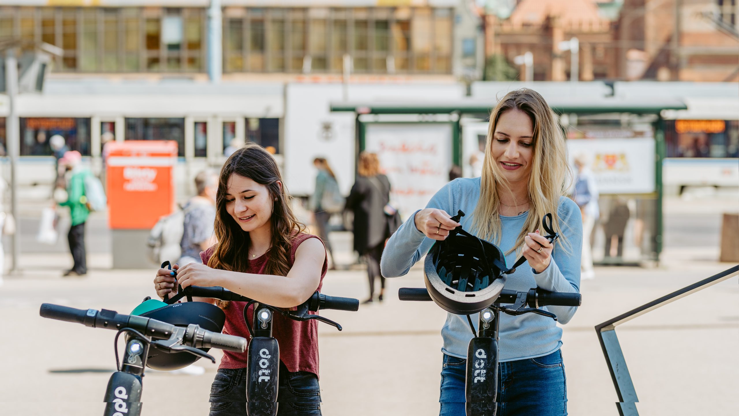 Two women standing at Dott scooters in a sunny European street getting ready to put their helmets on.